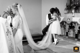 A touching moment captured at a Catholic Church in Malmesbury, Wiltshire, as the groom's daughter lovingly embraces her father after the ceremony, radiating warmth and family bonds.